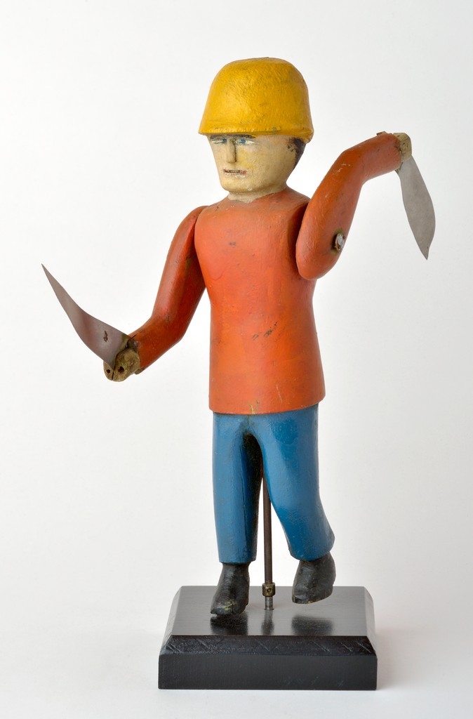 American polychrome carved wooden figural man whirligig with knife blade paddles on wooden stand, used as decoration in a butcher shop