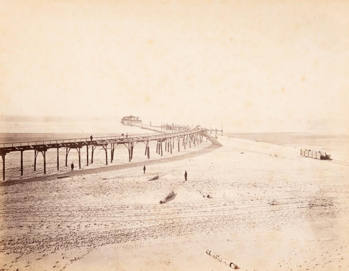 Noorderhavenhoofd met werksteiger in zee en stelling op het strand voor den aanvoer der betonblokken (1869)